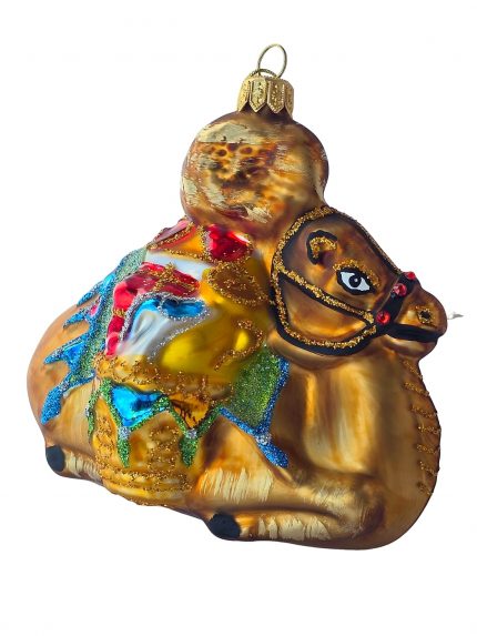 Stiklinis eglutės žaisliukas rudas kupranugaris – gulintis, galva į dešinę, su spalvingu balnu ir blizgučiais